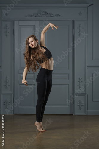 a girl with long hair in a black dance track rehearsing a dance in a ballet studio