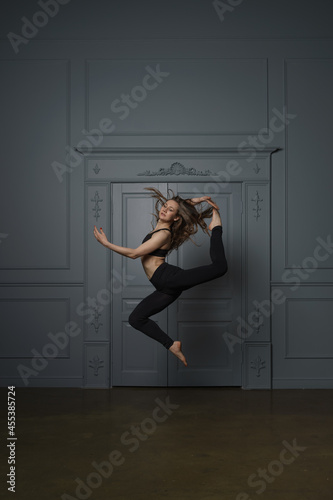 a girl with long hair in a black dance track rehearsing a dance in a ballet studio