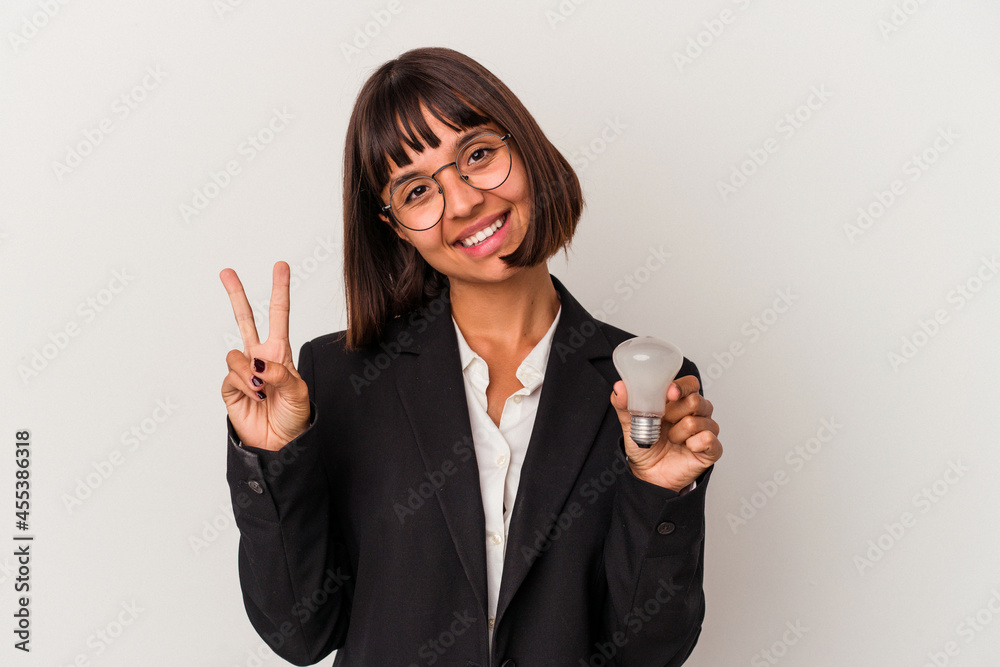 Young mixed race business woman holding a light bulb isolated on white background joyful and carefree showing a peace symbol with fingers. Young mixed race business woman holding a light bulb isolated on white background joyful and carefree showing a peace symbol with fingers.