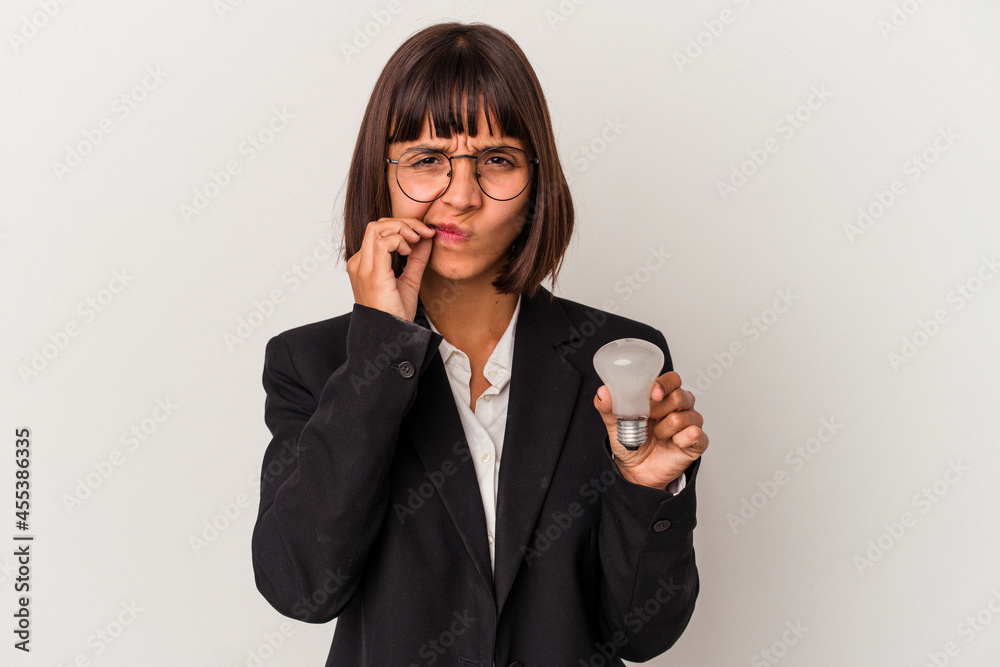 Young mixed race business woman holding a light bulb isolated on white background with fingers on lips keeping a secret.