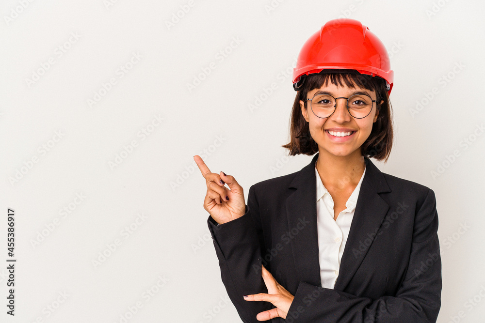 Young architect woman with red helmet isolated on white background smiling cheerfully pointing with forefinger away.