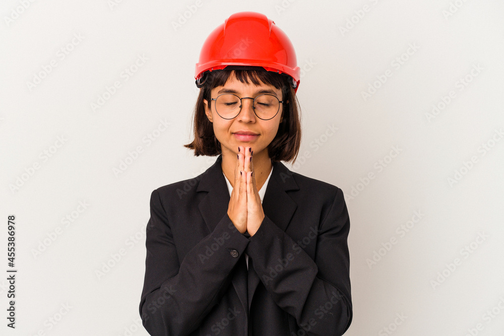 Young architect woman with red helmet isolated on white background holding hands in pray near mouth, feels confident. Young architect woman with red helmet isolated on white background holding hands in pray near mouth, feels confident.