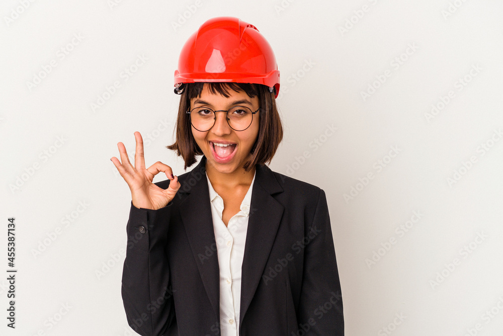 Young architect woman with red helmet isolated on white background winks an eye and holds an okay gesture with hand. Young architect woman with red helmet isolated on white background winks an eye and holds an okay gesture with hand.