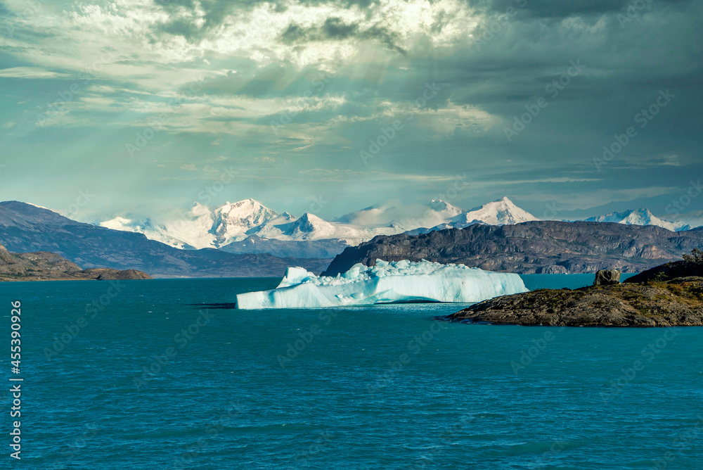 Floating iceberg on a lake in Patagonia, Argentina, with mountains and clouds in the background.
