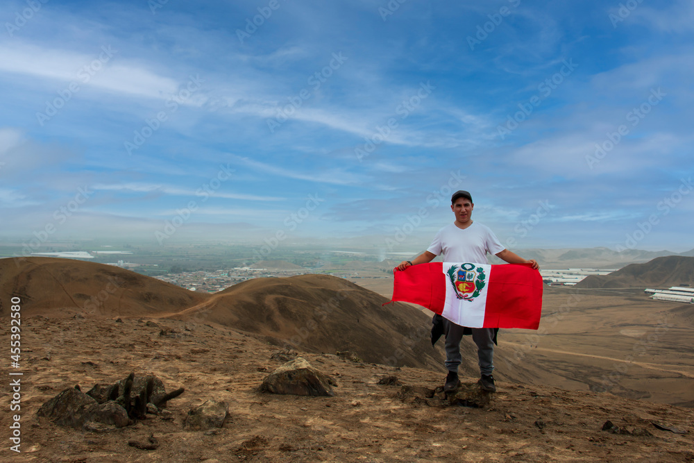 A man on vacation poses happily next to a Peruvian flag. Man gestures with the body. A man on vacation poses happily next to a Peruvian flag. Man gestures with the body.