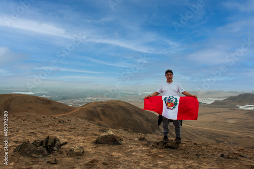 A man on vacation poses happily next to a Peruvian flag. Man gestures with the body.