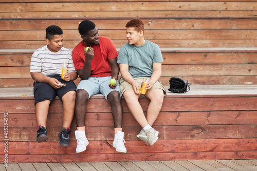 Quadro em tela Happy black father sitting on bleacher bench and holding tennis balls while chat