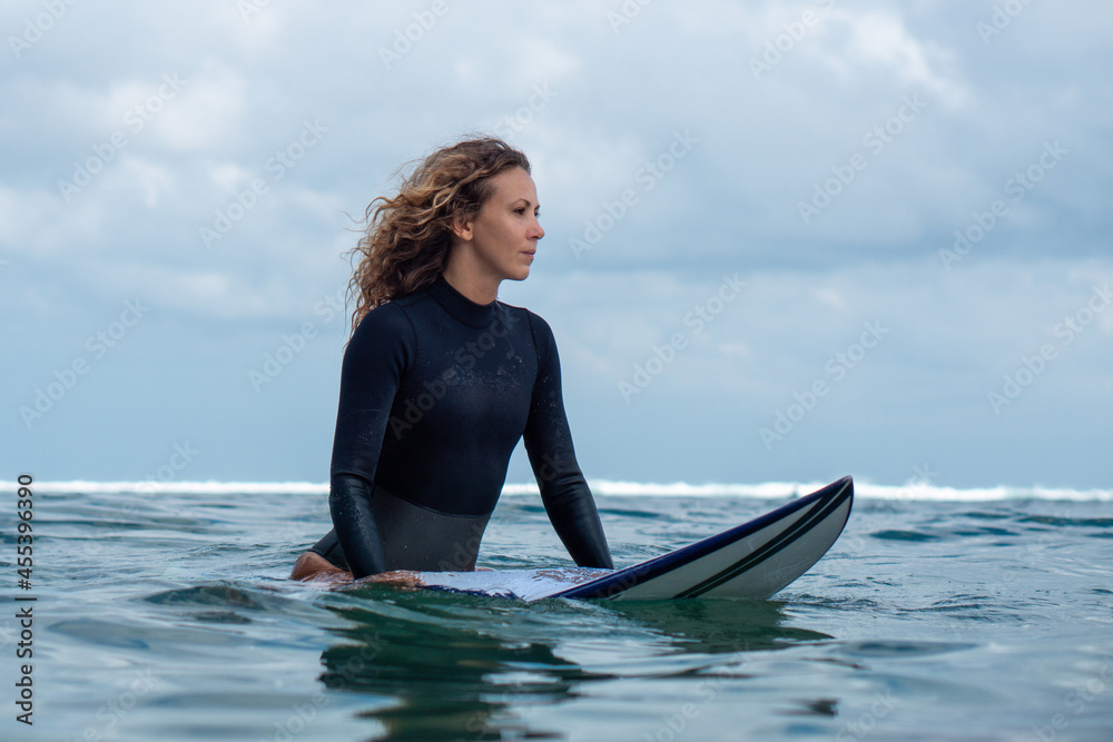 Portrait of surfer girl on white surf board in blue ocean pictured from the water Portrait of surfer girl on white surf board in blue ocean pictured from the water