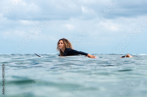 Portrait of surfer girl on white surf board in blue ocean pictured from the water © Lila Koan