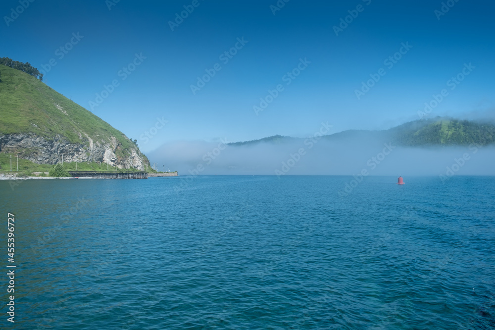 Lake Baikal close to village Port Baikal, Russia. Sunny day view of the high shore and clear lake water with fog