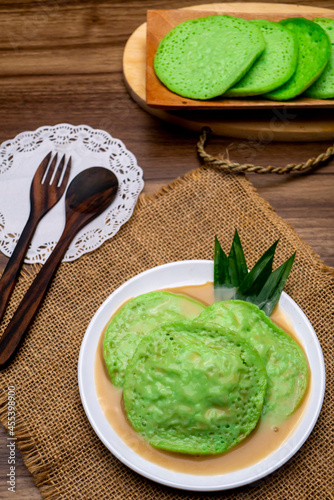Green Serabi or Surabi, Indonesian traditional food, with coconut milk and a mixture of brown sugar on wooden table and cultery