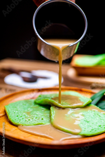 Green Serabi or Surabi, Indonesian traditional food, with coconut milk and a mixture of brown sugar on wooden plate 