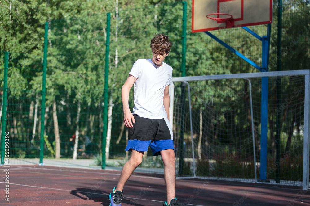 Cute teenager plays basketball at city playground. A boy holds basketball ball in his hands outside. Active life, hobby, sports for children Cute teenager plays basketball at city playground. A boy holds basketball ball in his hands outside. Active life, hobby, sports for children