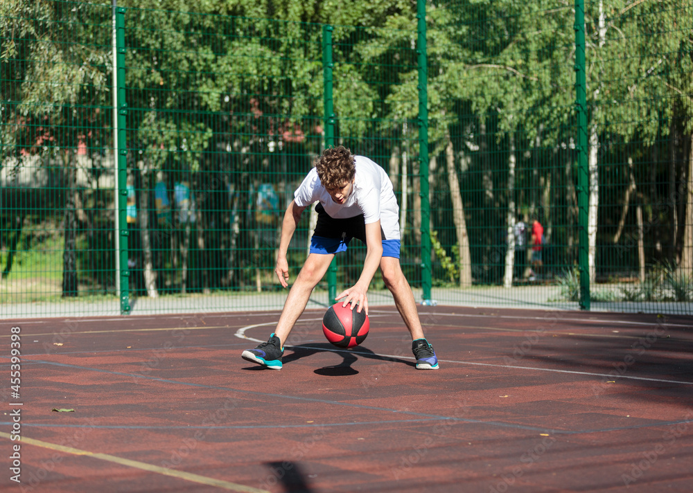 Cute teenager plays basketball at city playground. A boy holds basketball ball in his hands outside. Active life, hobby, sports for children	