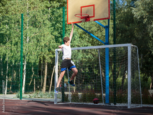 Cute teenager plays basketball at city playground. A boy holds basketball ball in his hands outside. Active life, hobby, sports for children  © Natali