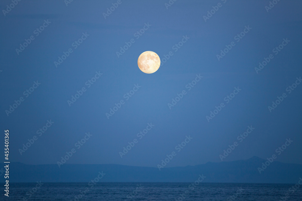 満月が知床の海から見る国後島の上に輝く