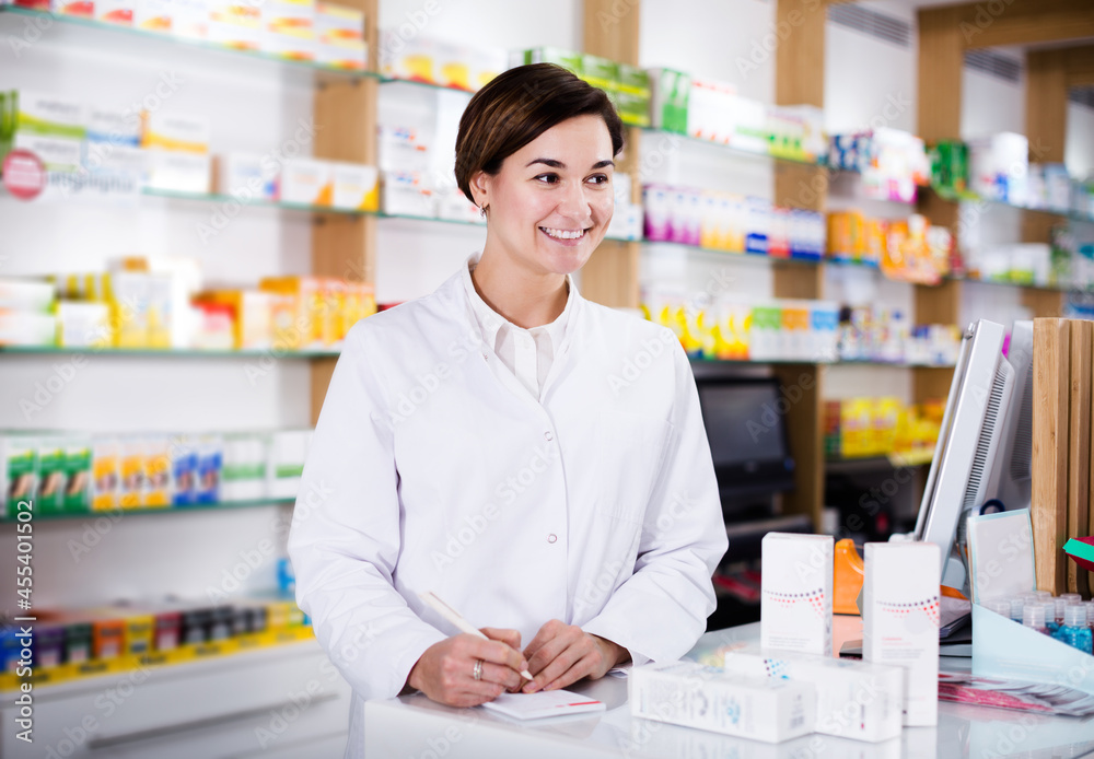 Glad young woman pharmacist ready to assist in choosing at counter in pharmacy