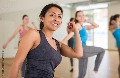 Cheerful hispanic woman practicing vigorous lindy hop movements in group dance class.