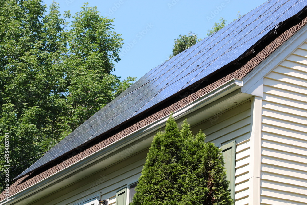 Solar panels on top of a house roof on a sunny summer day with blue sky and trees in the background Solar panels on top of a house roof on a sunny summer day with blue sky and trees in the background