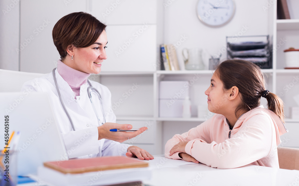 Doctor fills patient's card for girl and asks her about health in medical office
