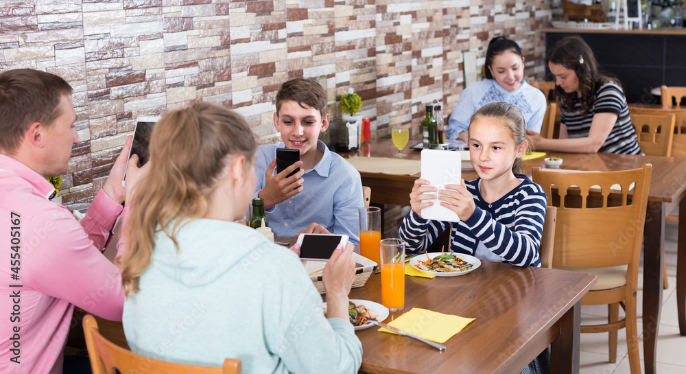 Obraz premium Modern family busying with phone during lunch in family cafe.