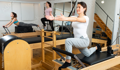 Young Hispanic woman performing set of pilates exercises on reformer in modern fitness studio