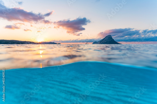 (Selective focus) Split-shot, over-under shot. Turquoise water in the foreground with Tavolara Island on the water surface during a stunning sunrise. Porto Taverna, Sardinia, Italy. © Travel Wild