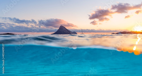 (Selective focus) Split-shot, over-under shot. Turquoise water in the foreground with Tavolara Island on the water surface during a stunning sunrise. Porto Taverna, Sardinia, Italy.