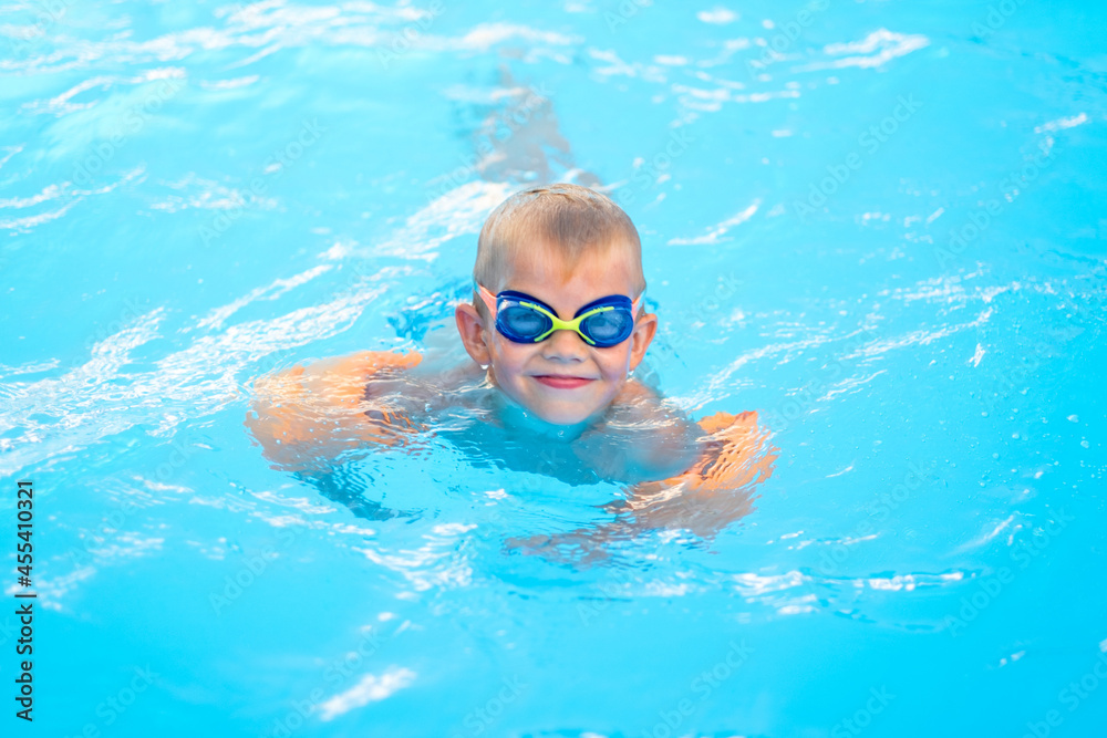 Portrait smiling boy in swimming pool, child in swimming glasses and inflatable sleeves. Summer travel hotel vacation or classes