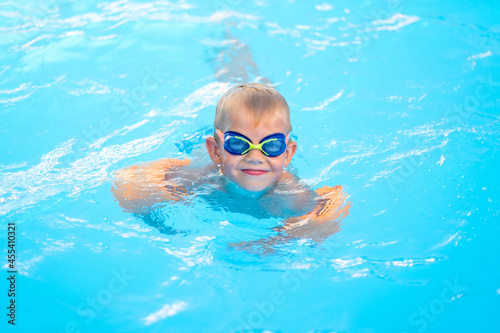 Portrait smiling boy in swimming pool, child in swimming glasses and inflatable sleeves. Summer travel hotel vacation or classes