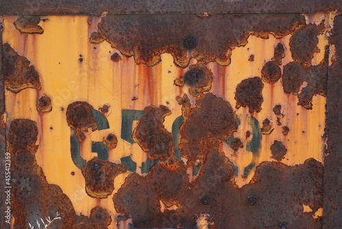 Discarded metal panel with flaking yellow paint and stenciled numbers obliterated by rust and holes photo