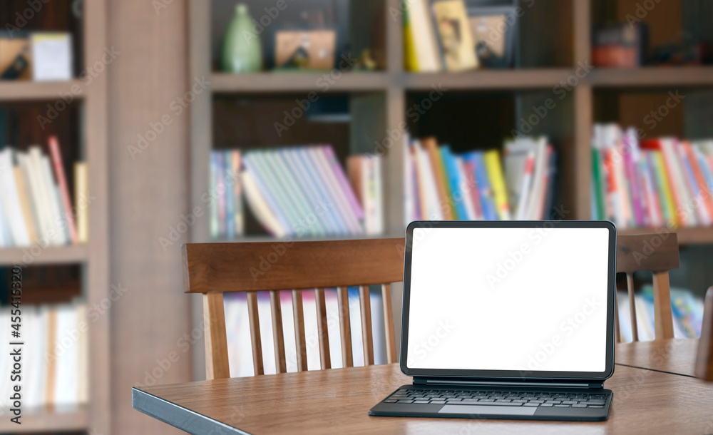 Mockup blank white screen tablet with magic keyboard on wooden table in library. Mockup blank white screen tablet with magic keyboard on wooden table in library.