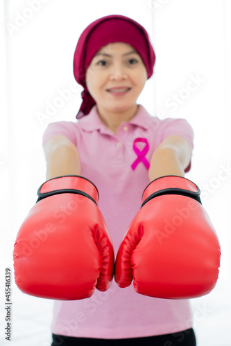 Asian woman on pink shirt with international ribbon sign of breast cancer awareness on chest and wearing red boxing glove expressing fighting support for health care against disease. © Bangkok Click Studio