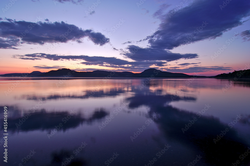 夜明けの空を湖面に反射する湖。日本の北海道の屈斜路湖で。