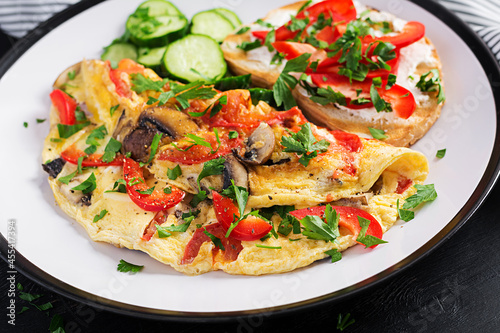 Omelette with mushrooms, paprika, tomatoes and sandwich with cream cheese on white plate. Frittata - italian omelet.