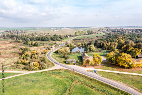 panoramic aerial view of rural landscape with green fields, forests, country roads and village in sunny autumn day.