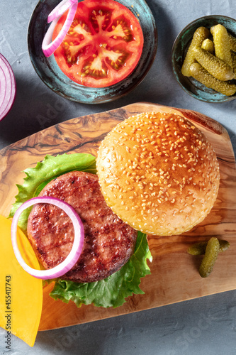 Hamburger recipe. Classic meat burger ingredients with a beef patty, sesame buns, tomato, onion, salad leaf and pickles, shot from the top
