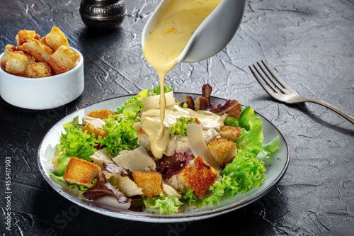 Tela Chicken Caesar salad with the classic dressing being poured, croutons, and peppe