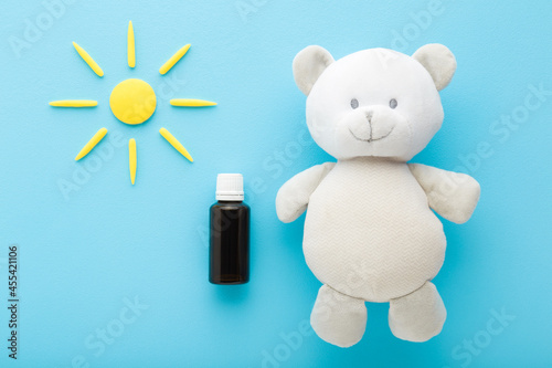 Brown glass bottle of d vitamin, white soft fluffy teddy bear and yellow sun shape on light blue table background. Pastel color. Closeup. Daily receiving vitamins for baby. Top down view. photo