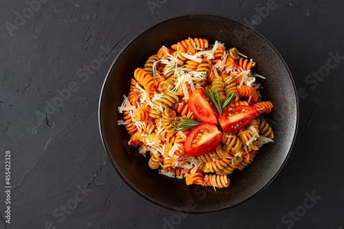 Italian dish, made of colored Fusilli pasta, in tomato sauce, with parmesan cheese and spices, top view, on a black background, no people,