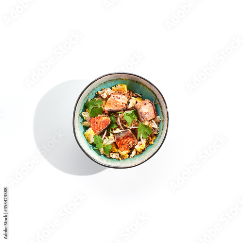 Asian traditional dish - fried rice with egg, vegetables, and salmon. Pan asian wok with rice, egg and fish on white background. Nasi goreng with salmon on isolated background with shadows.