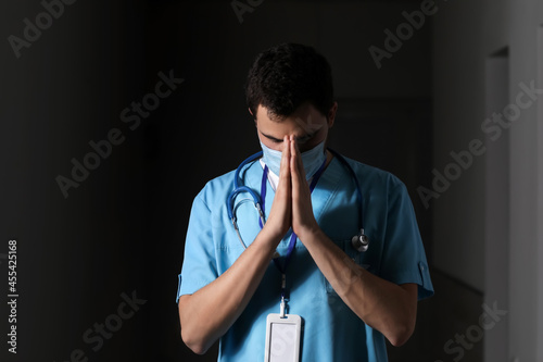 Praying male doctor on dark...