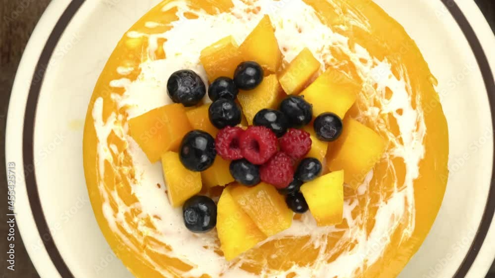 Top view zoom out of delicious homemade mango cheesecake garnished with pieces of ripe mango, preserved raspberry and blueberry in brown ceramic dish with moka pot coffee maker and serving shovel. Top view zoom out of delicious homemade mango cheesecake garnished with pieces of ripe mango, preserved raspberry and blueberry in brown ceramic dish with moka pot coffee maker and serving shovel.