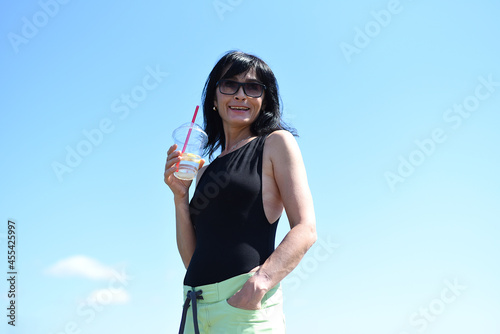 45 years old Russian woman drinking lemonad and standing against blue sky