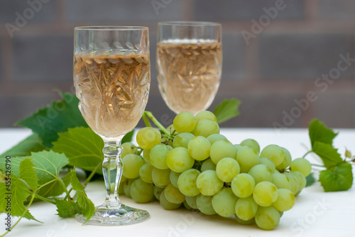 Two glasses of white wine, bunches of grapes and a young vine on a light wooden background. A horizontal snapshot.