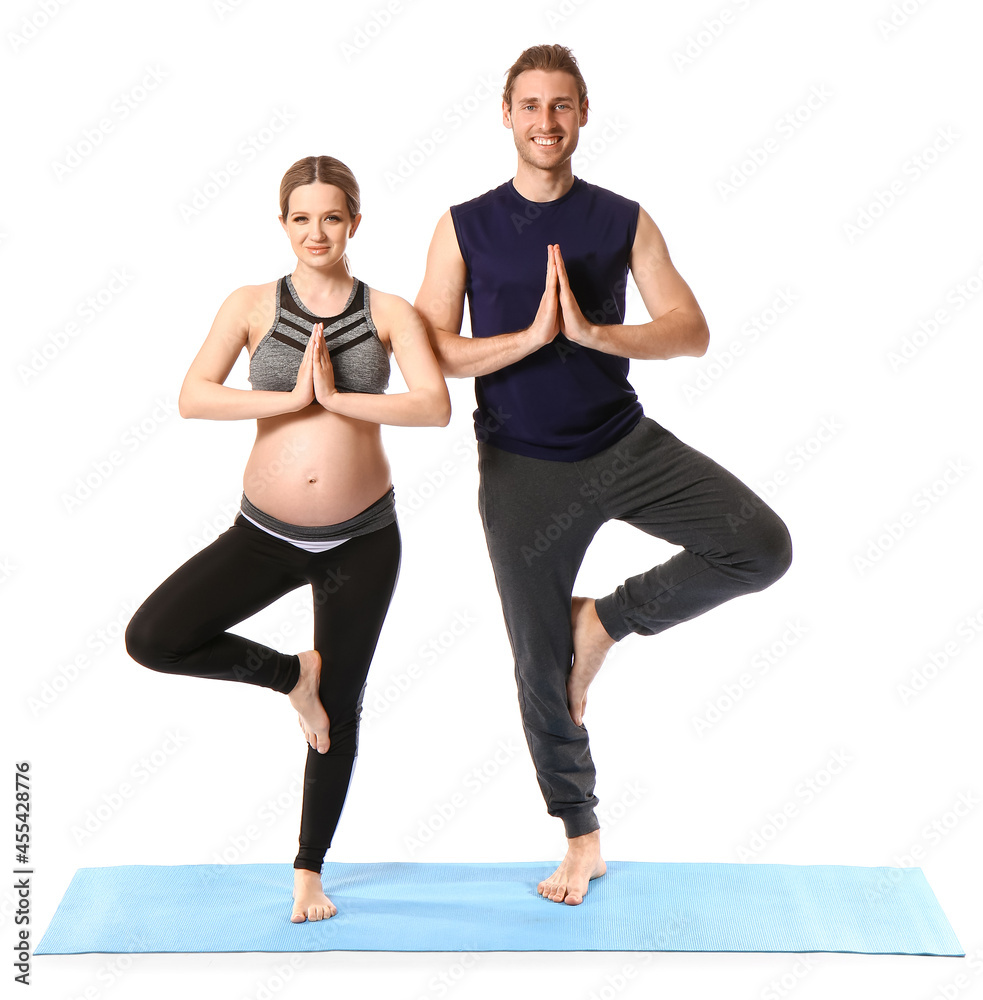 Obraz premium Young pregnant woman and her husband practicing yoga on white background