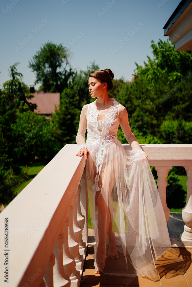 Fototapeta premium a beautiful bride in a transparent lace robe stands on the terrace.