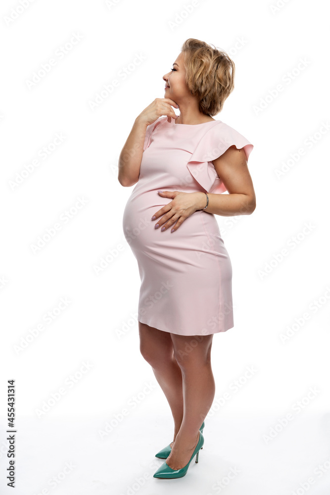 Beautiful pregnant woman in a pink dress. Smiling blonde future mom. Tenderness in anticipation of the baby. Isolated on white background. Vertical. Full height. Beautiful pregnant woman in a pink dress. Smiling blonde future mom. Tenderness in anticipation of the baby. Isolated on white background. Vertical. Full height.