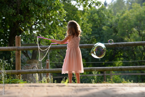 Sommertag. Kleines Mädchen im rosa Kleid spielt mit Seifenblasen