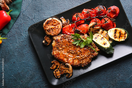 Plate with tasty pork steak and vegetables on dark background